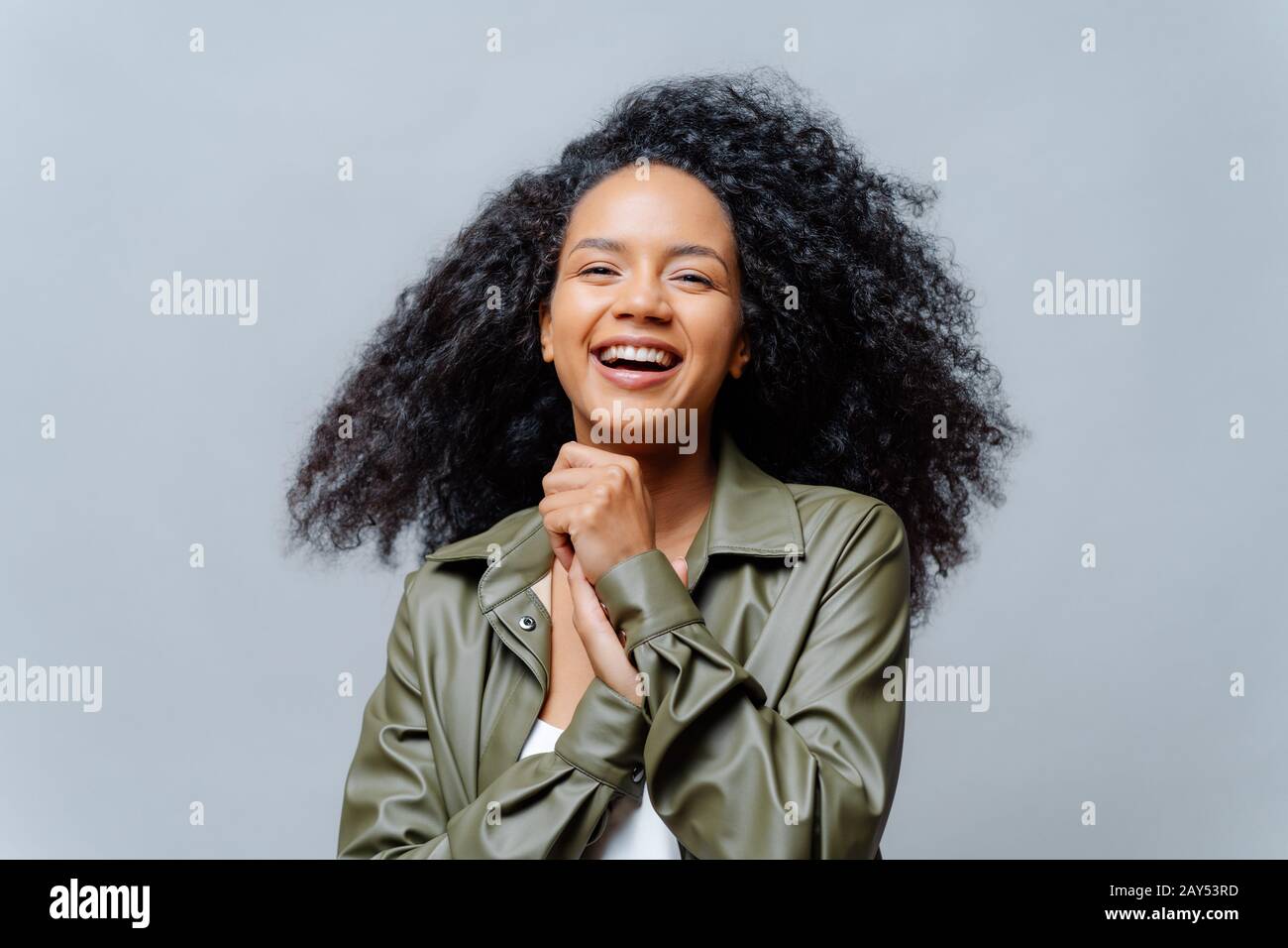 Une femme mauve sombre et surplaisante rie avec joie, riant avec une drôle de blague, maintient les mains enfoncées ensemble, vêtues de vêtements à la mode, isolée sur g Banque D'Images