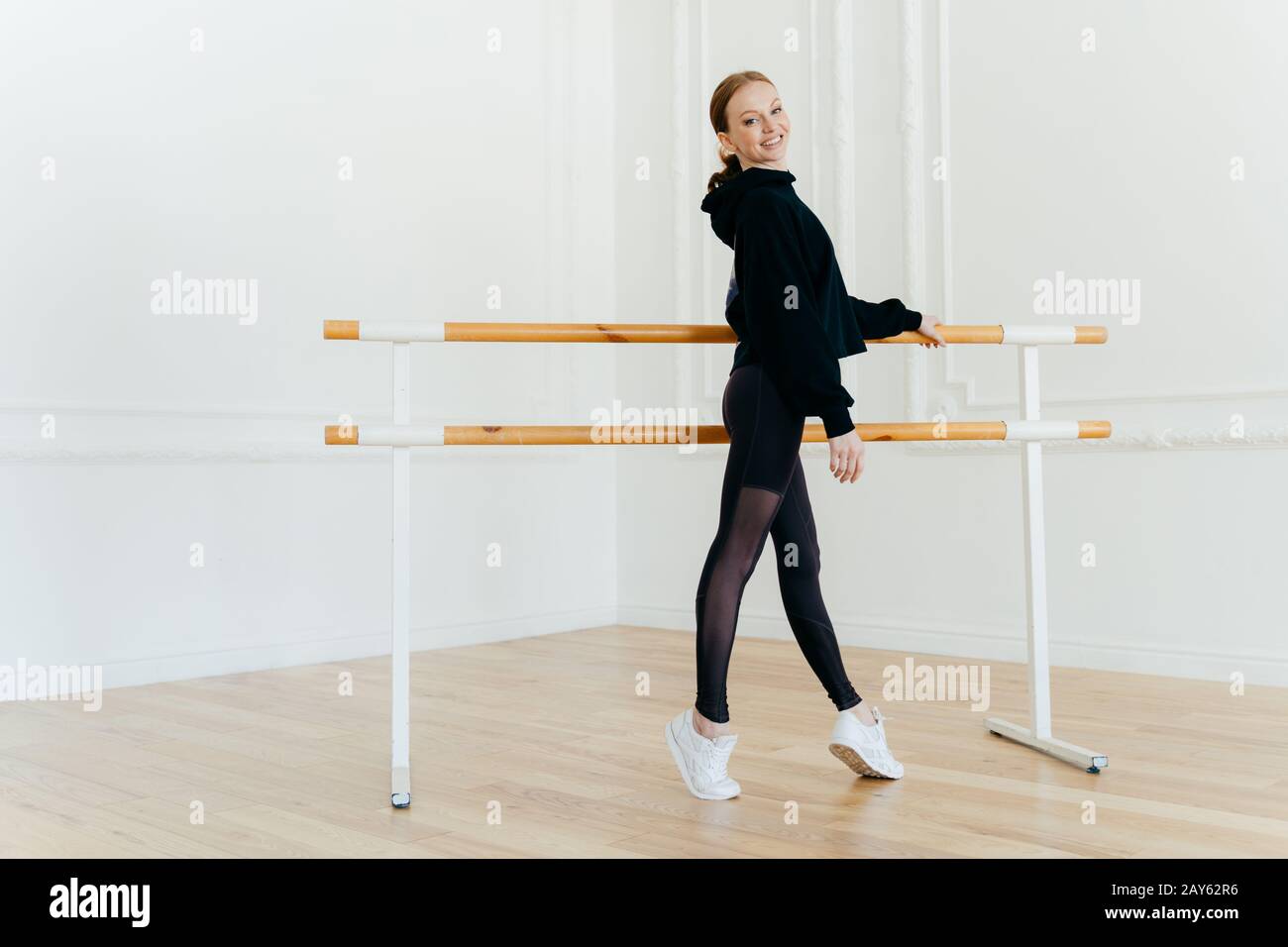 La jeune femme aux cheveux rouges mince se tient sur les orteils de la pointe, étant en bonne forme de corps, s'entraîne tous les jours, porte un sweat-shirt noir, des leggings et wh Banque D'Images