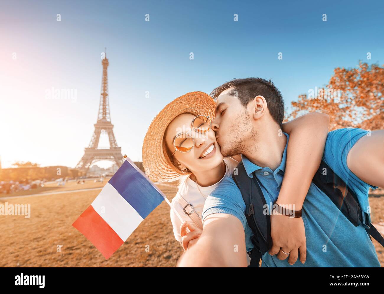 Couple mixte de course amoureux embrassant et prenant selfie avec drapeau français et tour Eiffel en arrière-plan. Voyage de lune de miel en France et Paris concept Banque D'Images