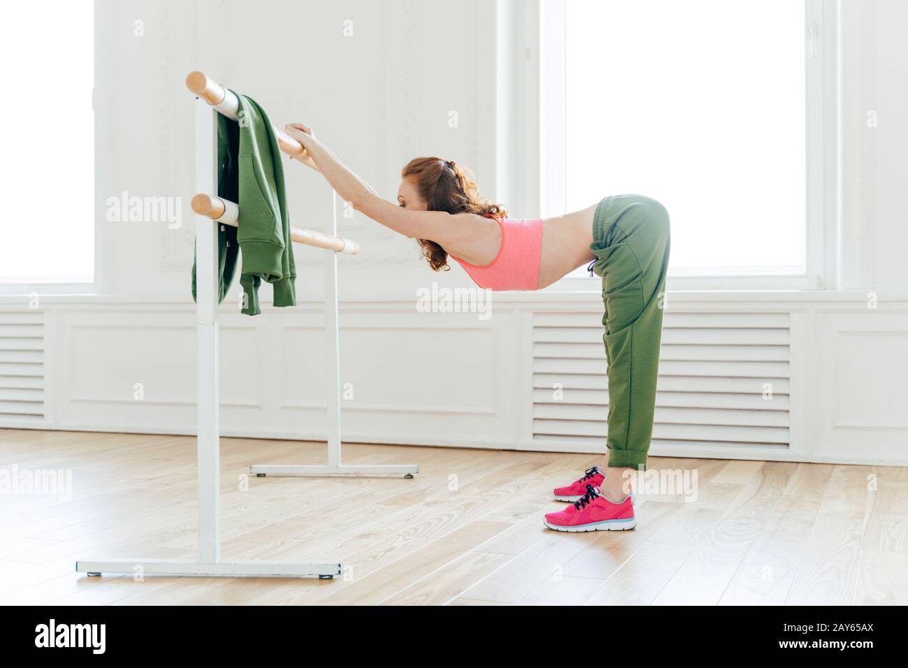 Tir intérieur de sportif dans le sport et l'habillement actif, penche à la barre de ballet, a une séance d'entraînement productive, forme mince du corps, étire les muscles, h Banque D'Images