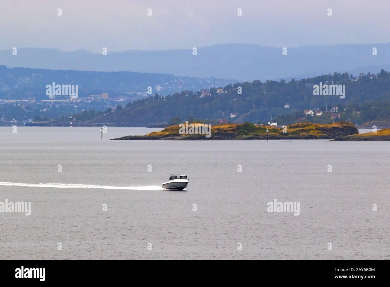 Bateau à moteur en vitesse au large de l'îlot côtier avec de petits cottages dans le fjord intérieur d'Oslofjord, Oslo est à distance, Norvège sur une sombre journée d'août Banque D'Images