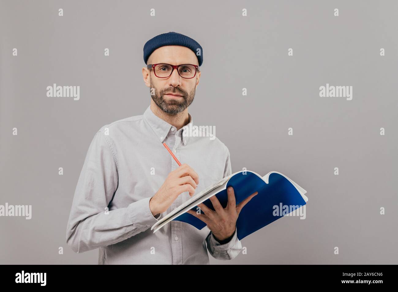 Coup d'isolé mâle confiant auteur creats nouveau roman, est titulaire d'un crayon et un bloc-notes, écrit des notes et d'idées, porte des verres optiques, pose plus de Banque D'Images