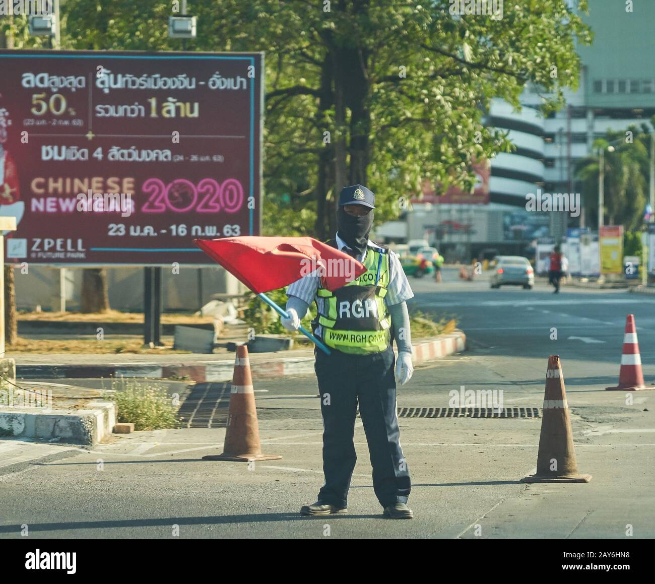 Un garde de sécurité avec un drapeau rouge, portant un masque facial, devant un panneau d'affichage chinois du nouvel an. Banque D'Images
