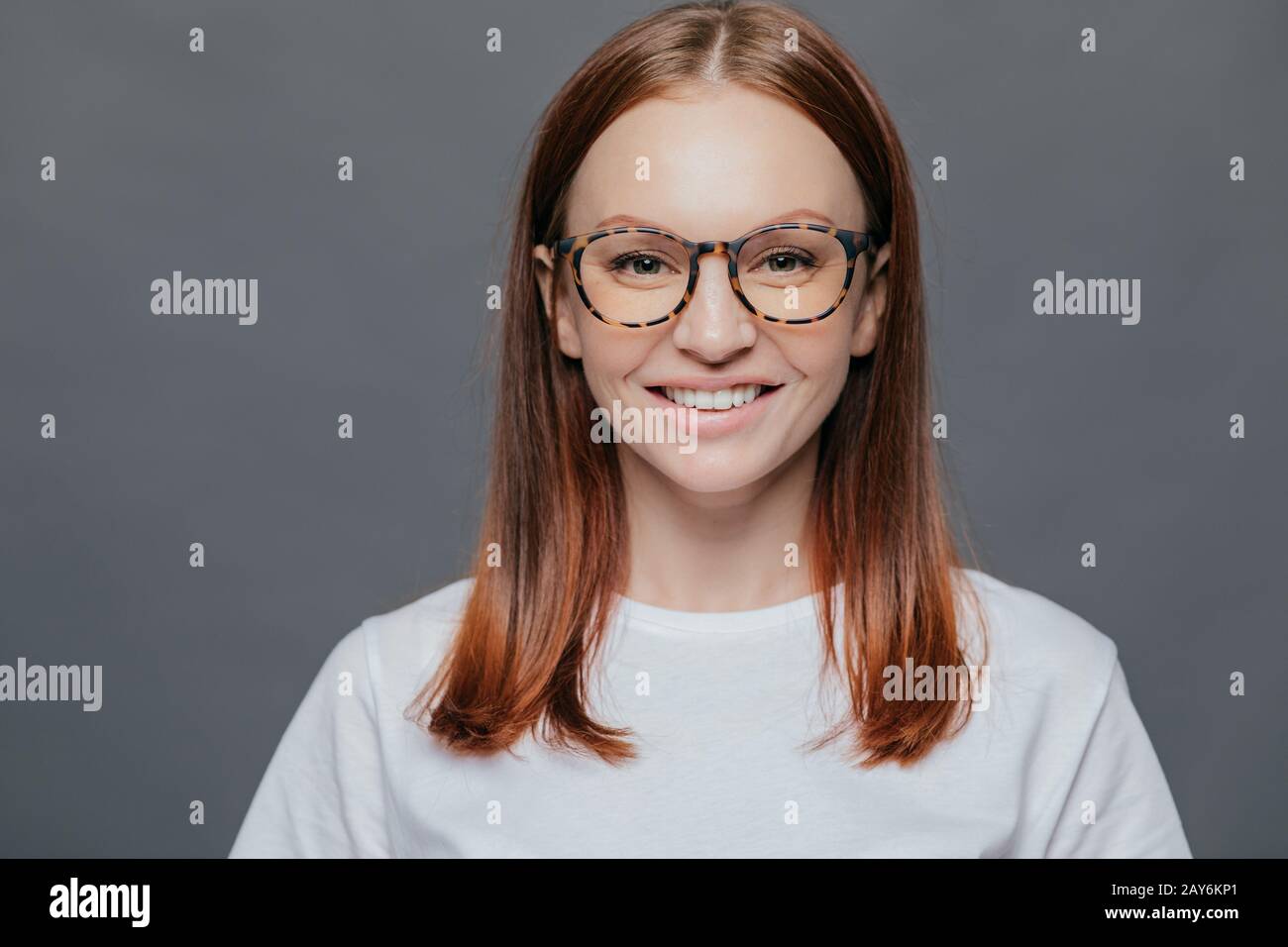 Portrait d'agréable à la jeune femme aux cheveux noirs porte des verres transparents, vêtu de vêtements décontractés, a une peau, oeil positif, montre whit Banque D'Images