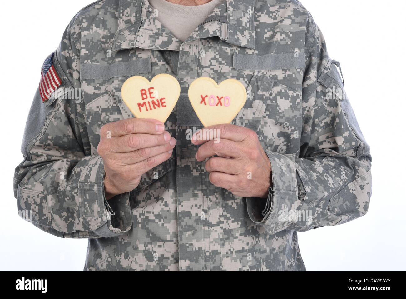 Gros plan d'un soldat tenant deux biscuits de la Saint Valentin en forme de coeur avec les mots Be Mine et XOXO écrits en givrage rouge. Banque D'Images