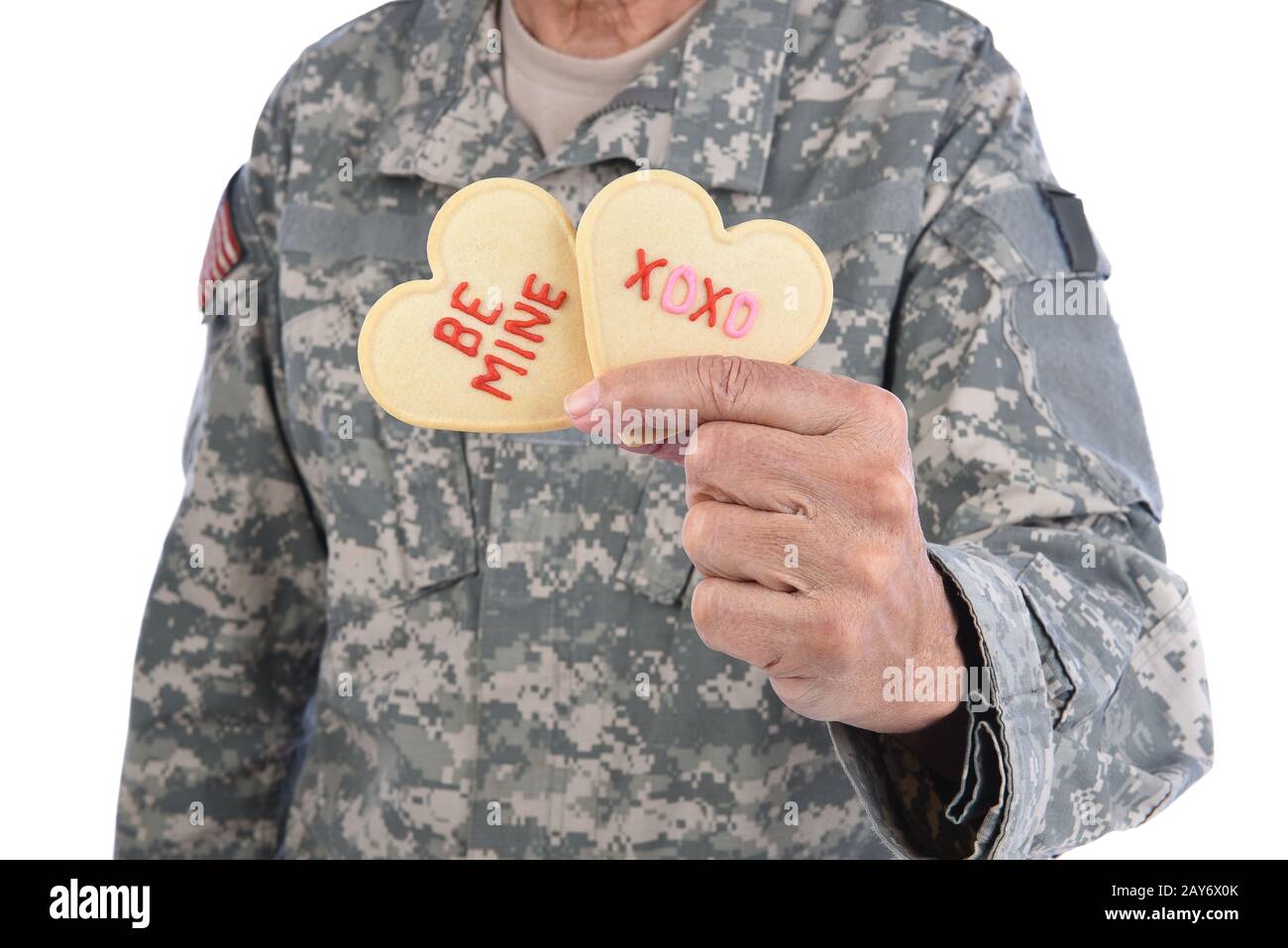 Gros plan d'un soldat tenant deux biscuits de la Saint Valentin en forme de coeur dans une main avec les mots Be Mine et XOXO écrits en givrage rouge. Banque D'Images