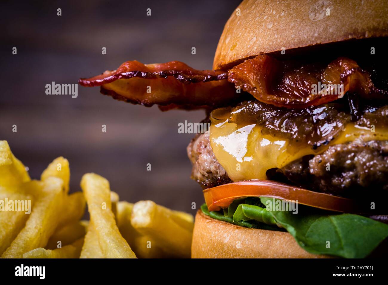 Hamburger de bœuf artisanal avec fromage, bacon, feuilles de roquette, caraméliser l'oignon et les frites sur table en bois et fond rustique Banque D'Images