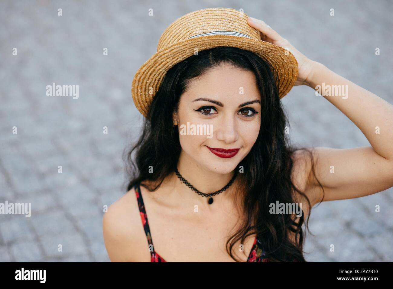 Portrait extérieur d'une femme brunette aux yeux sombres, lèvres rouges et peau saine portant un chapeau d'été, en gardant sa main sur la tête, se reposer pendant la marche Banque D'Images