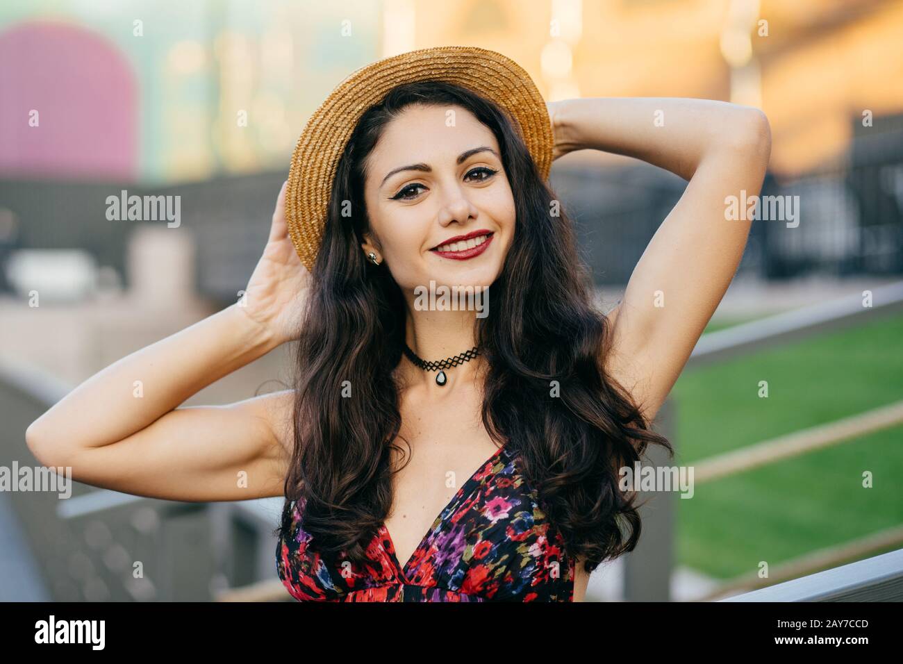 Femme brunette reposante avec un beau remake portant un chapeau d'été et une robe en gardant la main derrière sa tête se sentant plaisir tout en passant son été Banque D'Images