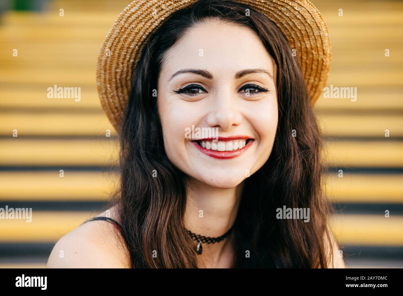 Jeune femme brunette aux yeux sombres et brillants, lèvres bien formées et grand sourire portant un chapeau de paille d'été assis dans les escaliers. Féeli émotionnelle féminine Banque D'Images