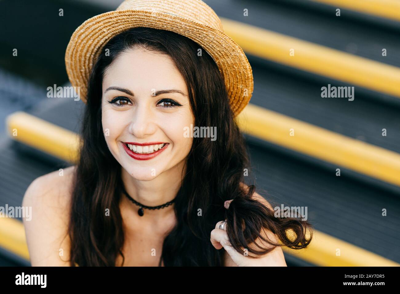 Femme heureuse avec des cheveux luxueux, de charmants yeux lumineux, des lèvres rouges bien formées et une peau pure touchant avec la main ses cheveux, portant un chapeau d'été, smilin Banque D'Images