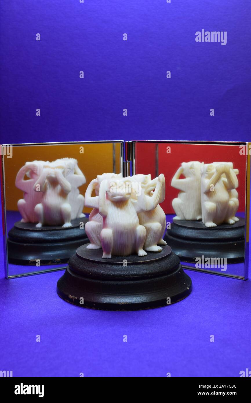 Trois singes sculptés blancs sages se trouvent devant un double miroir pour refléter toutes les postures des singes. Fond bleu, orange et jaune dans les miroirs Banque D'Images