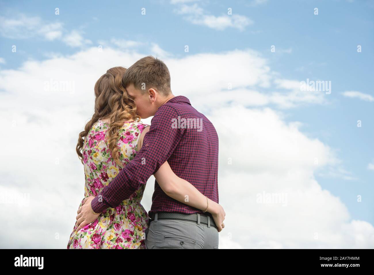 Vue de l'arrière. Jeune couple embrassant baisers contre le ciel bleu et les nuages blancs. Banque D'Images