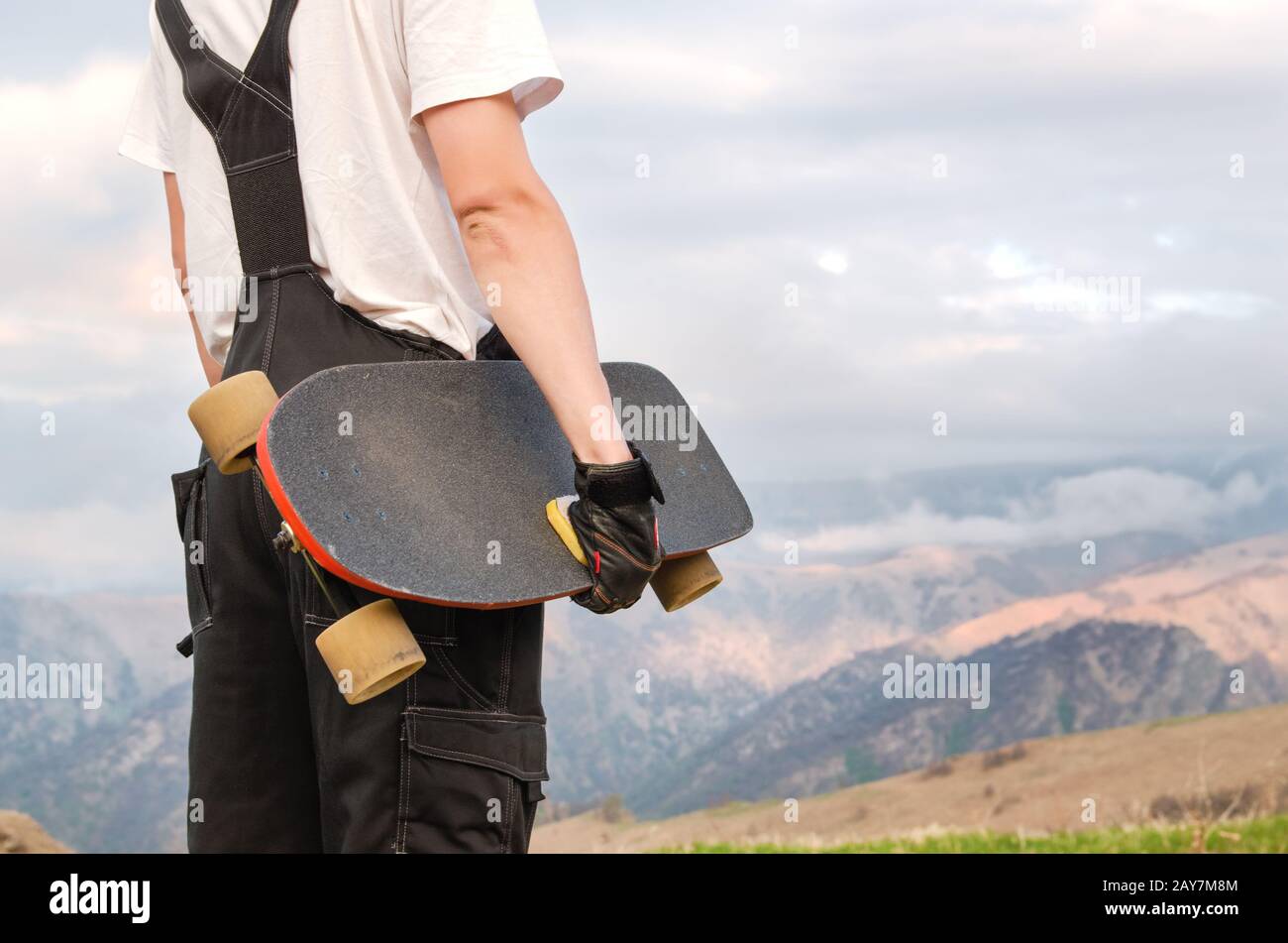 Un jeune homme dans un casque portant des gants avec une planche dans ses mains et vêtu d'un combo se tient sur un précipice haut dans le mounta Banque D'Images