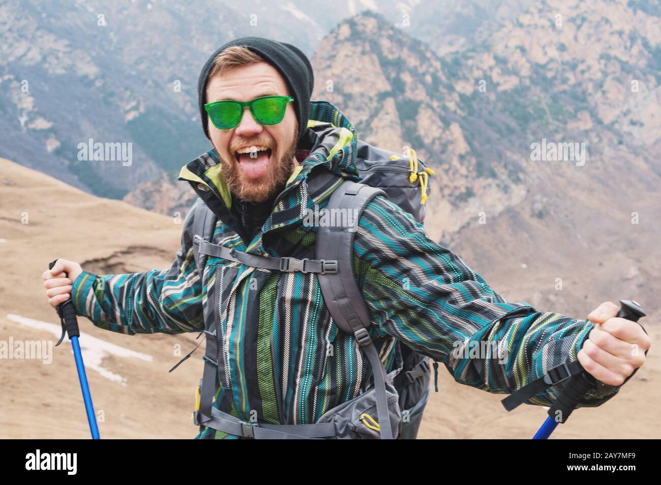 Un gars qui ressemble à un hipster montre sa langue et hurle dans les montagnes, étirant ses mains dans différentes directions Banque D'Images