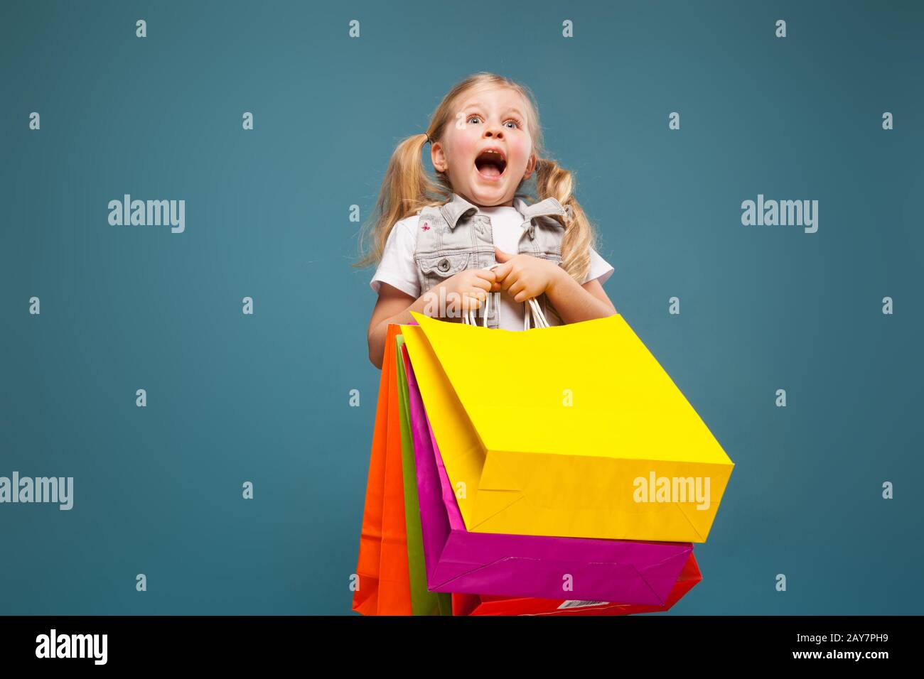 Adorable petite fille dans une chemise blanche, une veste blanche et un short blanc tiennent des sacs en papier colorés Banque D'Images