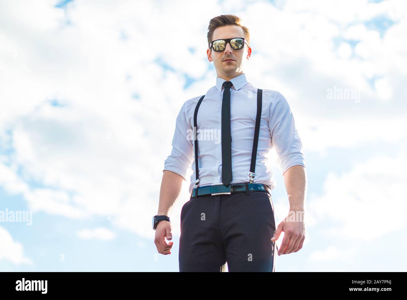 Jeune homme sérieux en chemise blanche, cravate, bretelles et lunettes de soleil Banque D'Images