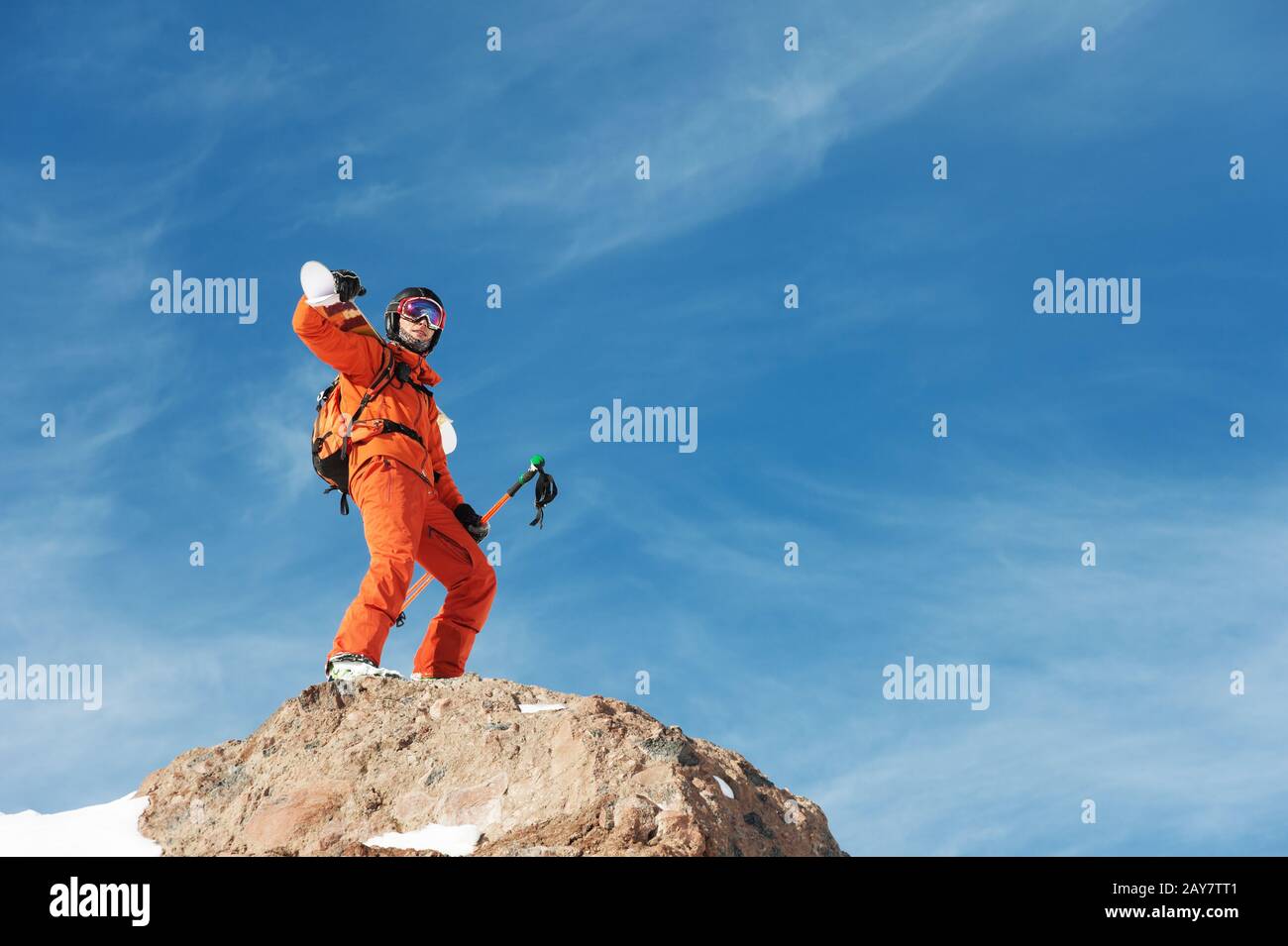 Portrait d'un Skieur dans un ensemble orange avec un sac à dos sur son dos et des skis sur ses épaules dans un casque se tient sur un agai de roche Banque D'Images