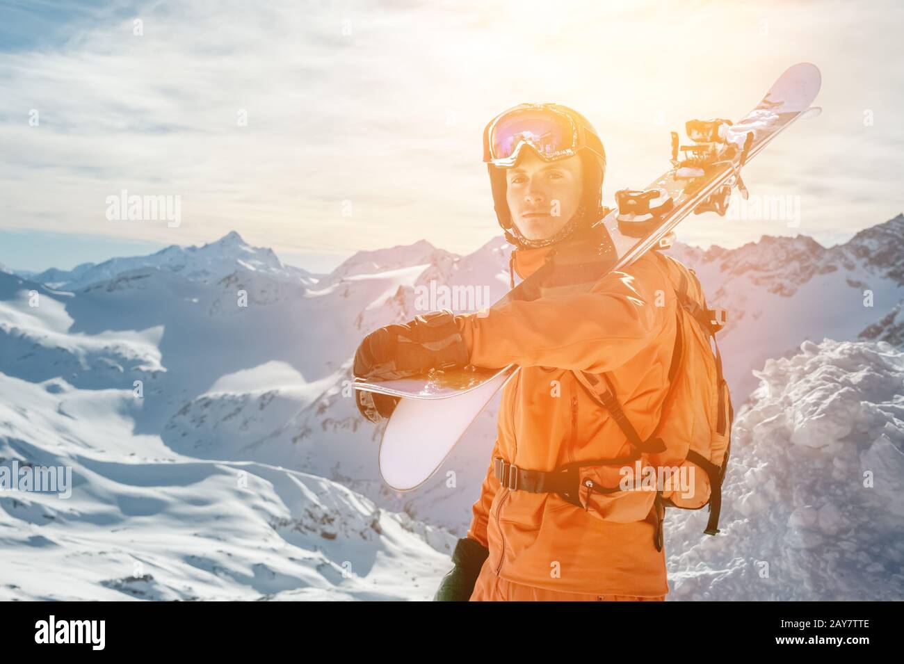 Portrait d'un Skieur dans un ensemble orange avec un sac à dos sur son dos et des skis sur ses épaules dans un casque se tient sur un agai de roche Banque D'Images