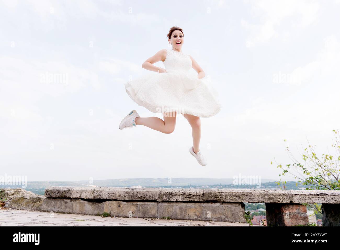 La folle mariée saute et s'accroche dans le ciel en toile de fond du paysage urbain d'une petite station balnéaire dans le nord du Caucase Banque D'Images