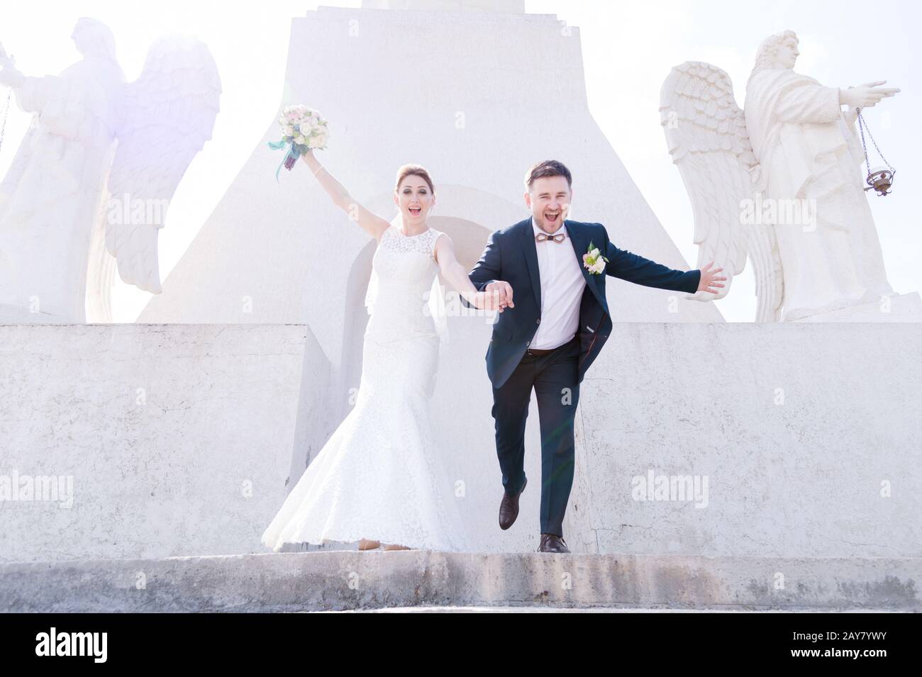 Portrait d'un couple charmant de jeunes mariés lors d'une journée de mariage avec un bouquet dans les mains qui descendent dans les escaliers en riant et souriant un Banque D'Images