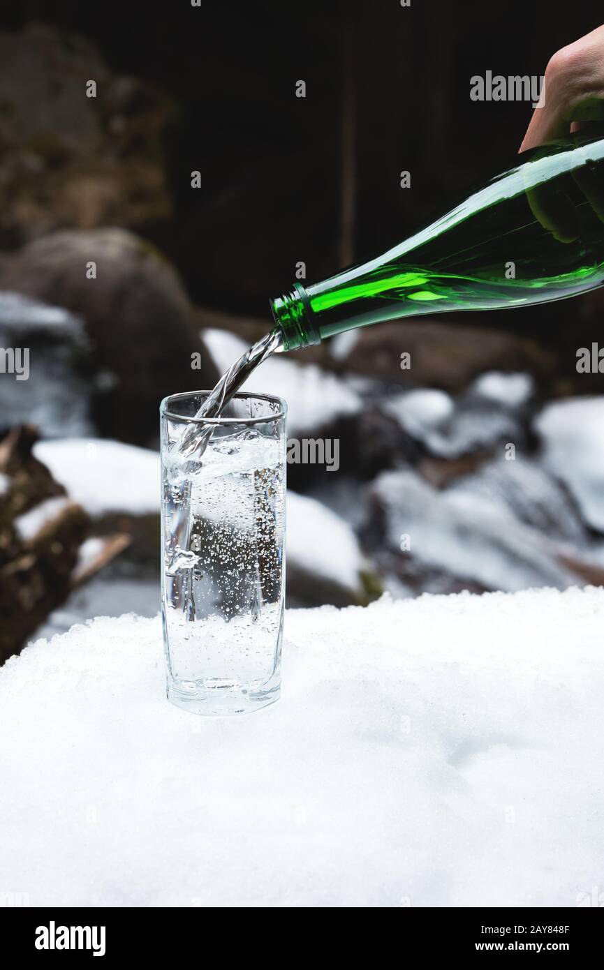 L'eau minérale minérale est versée à partir d'une bouteille verte en verre dans un bécher en verre transparent. Banque D'Images