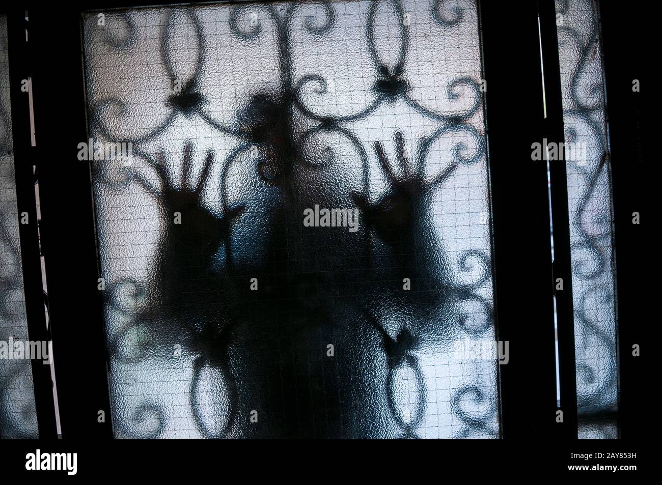 Figure de mystérieuse étranger en appuyant les mains contre une porte en verre texturée avec des barres de sécurité Banque D'Images