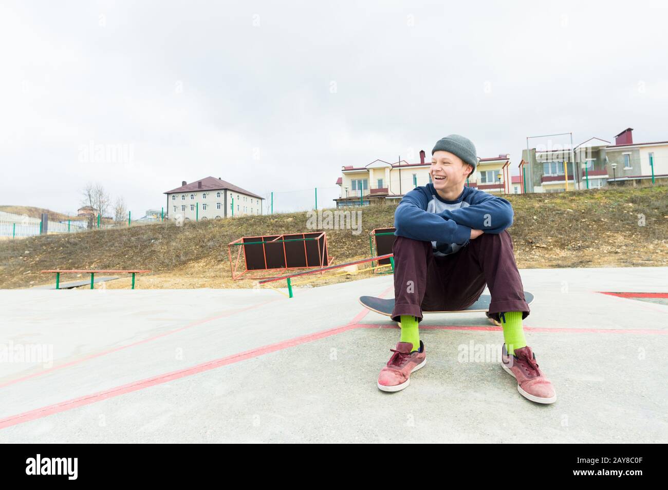 Un adolescent est assis sur un skateboard dans le parc et souriant. Le concept de temps libre passe pour les adolescents dans la ville Banque D'Images
