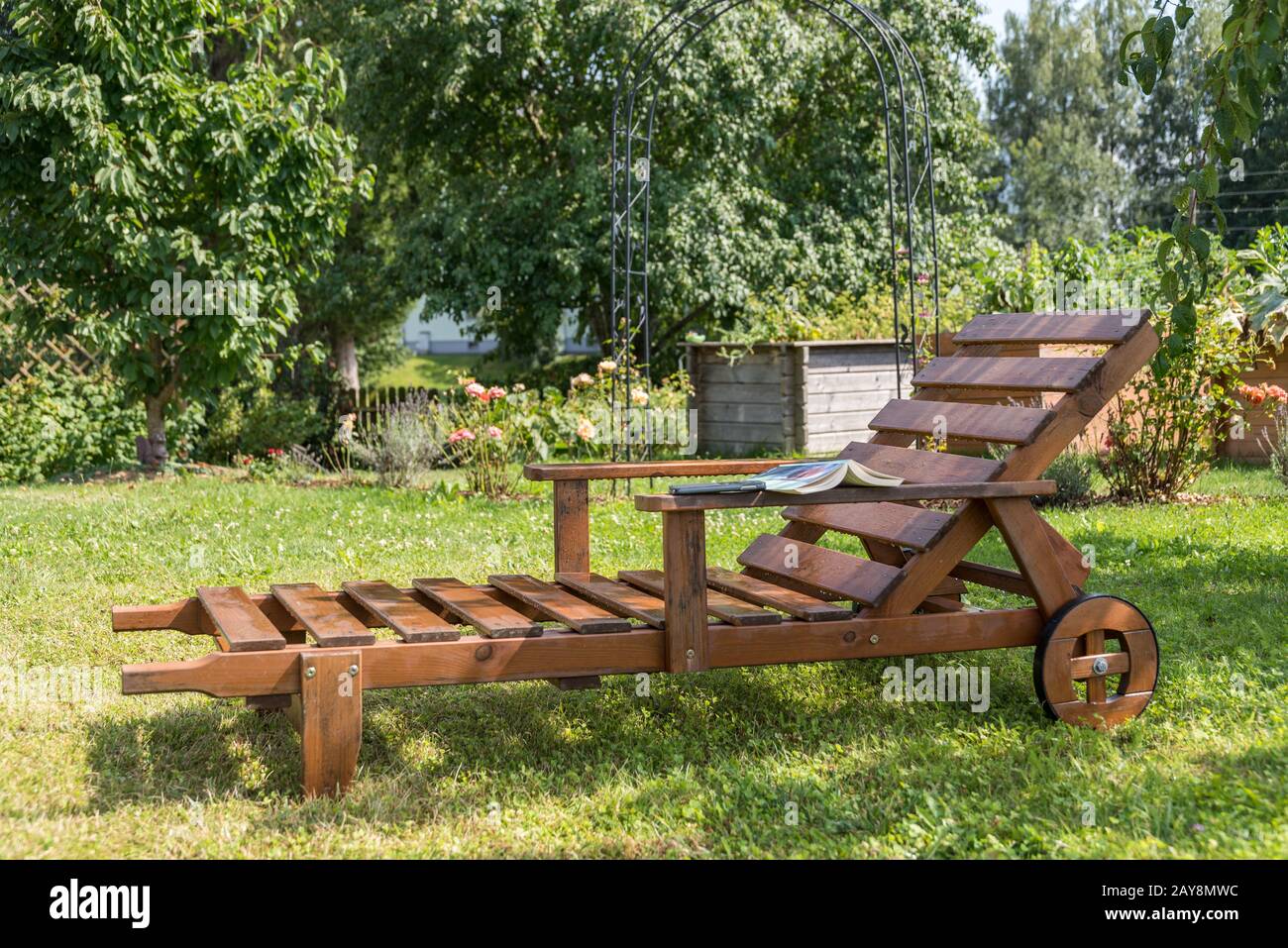Chaise longue en bois durable dans un jardin romantique avec un livre Banque D'Images