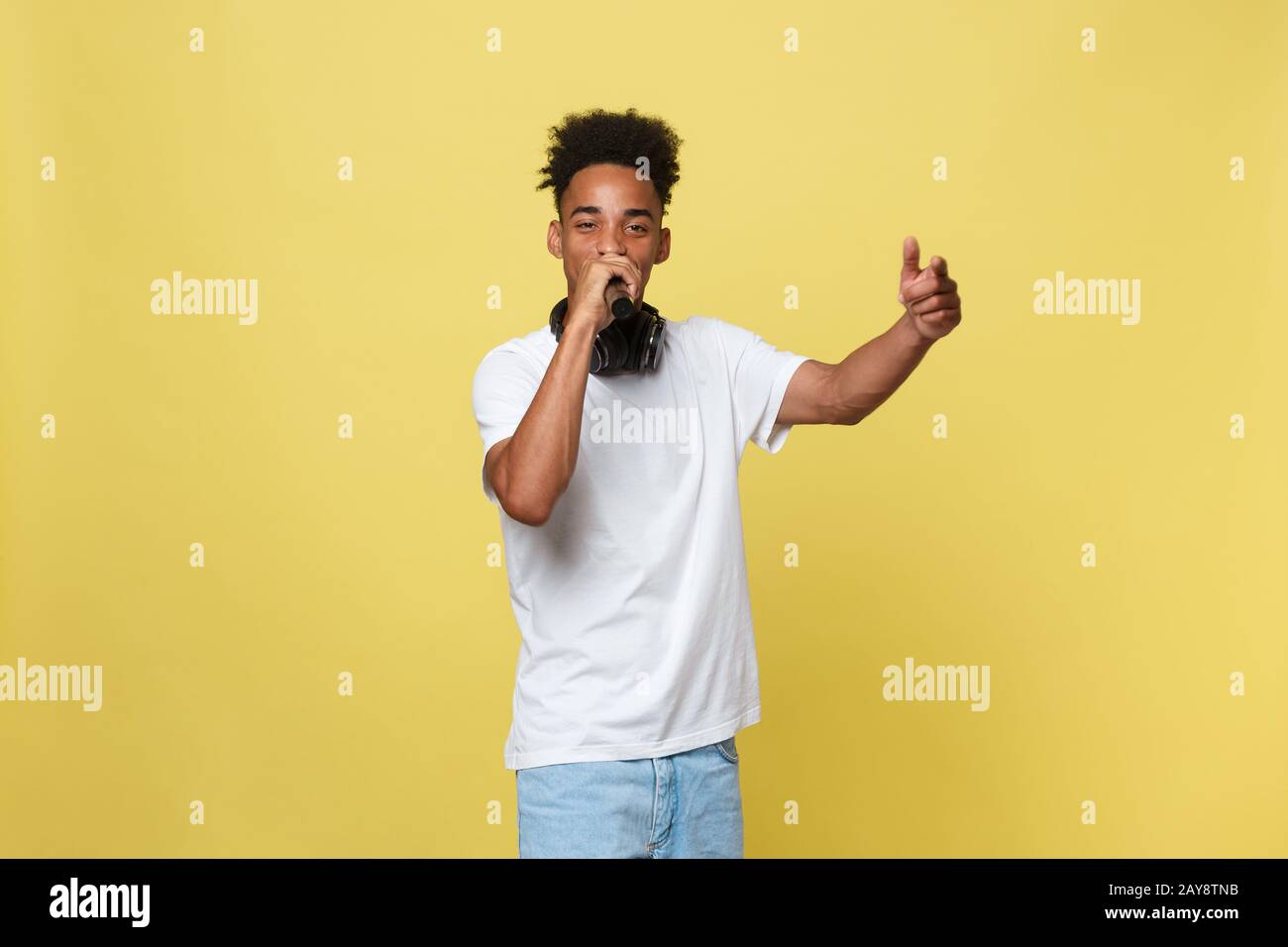 Joli jeune homme à peau foncée avec coupe afro en t-shirt blanc, gestuelle avec les mains et le microphone, danse et singi Banque D'Images