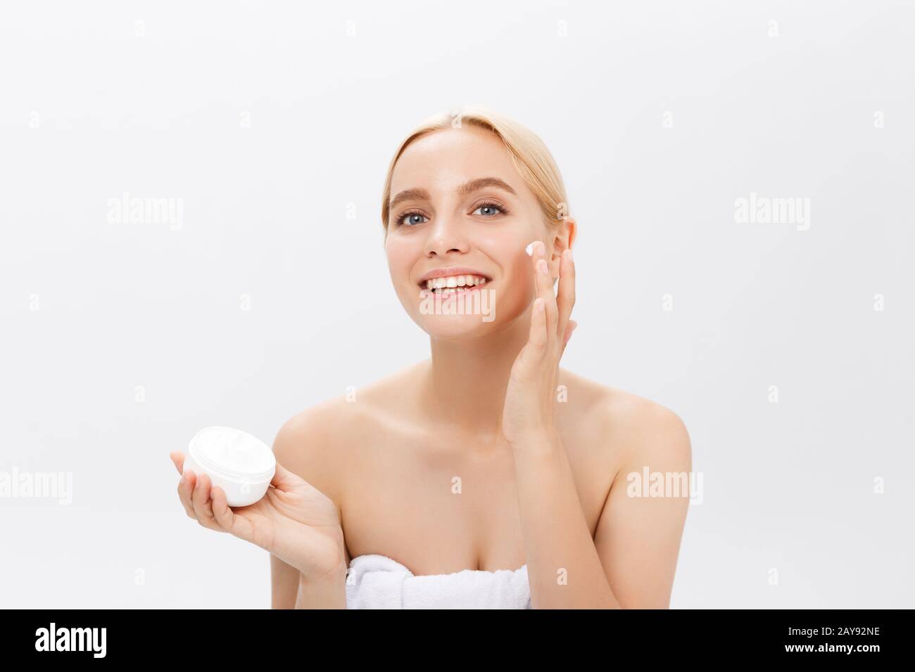 Beau modèle appliquant crème cosmétique traitement sur son visage on white Banque D'Images