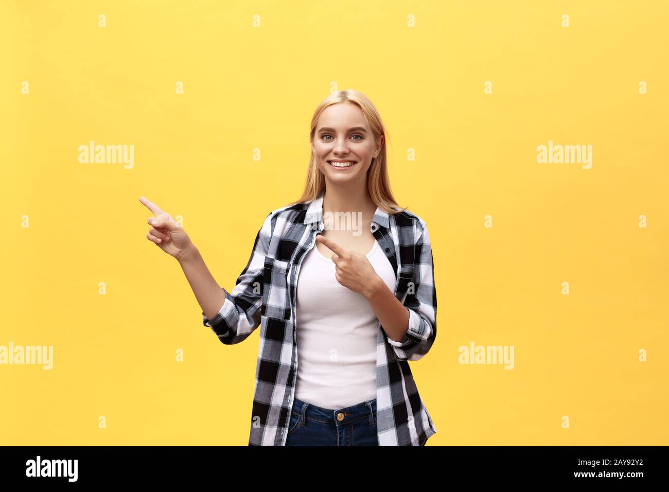 Laughing young woman in t-shirt à la recherche et à l'écart de pointage avec pouce sur fond jaune Banque D'Images