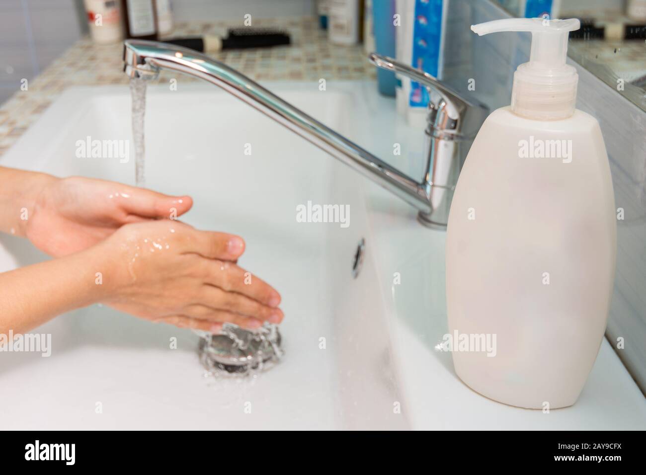 L'enfant se lave les mains sous le robinet, à l'avant-plan d'un tube de savon liquide Banque D'Images