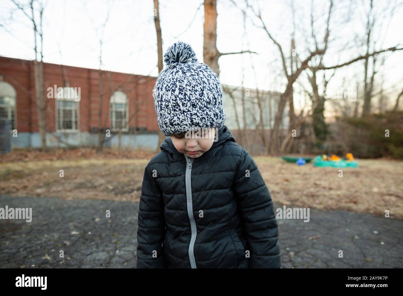 Un tout-petit garçon portant un chapeau d'hiver regarde vers le bas en se tenant dans l'allée Banque D'Images