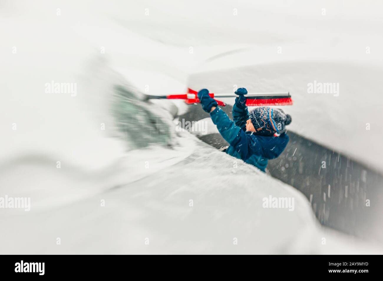 un garçon de 7 ans dépare le pare-brise de la neige pendant une tempête de neige Banque D'Images