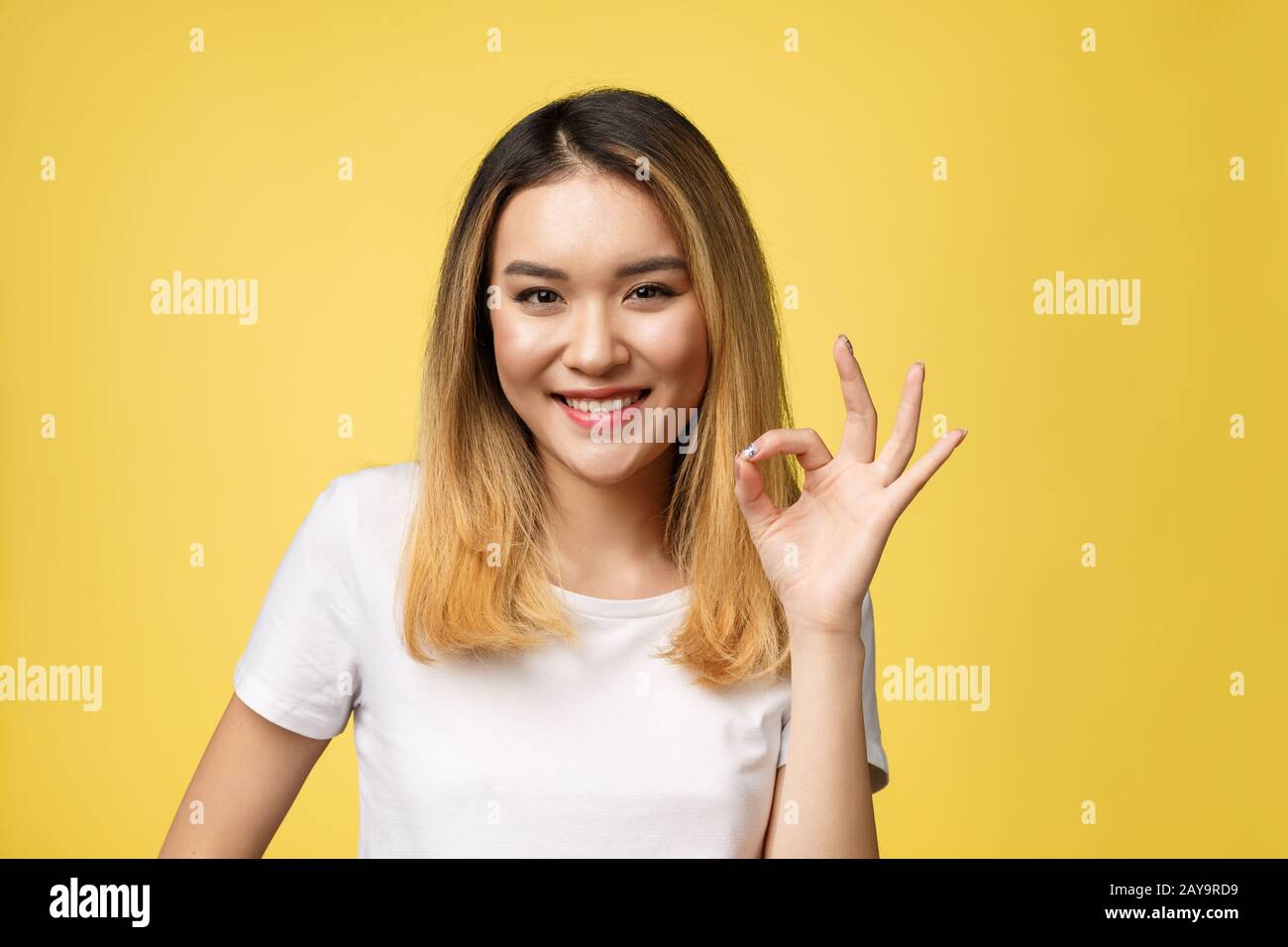 Jeune femme asiatique avec des gestes plus isoler signe ok fond jaune. Banque D'Images