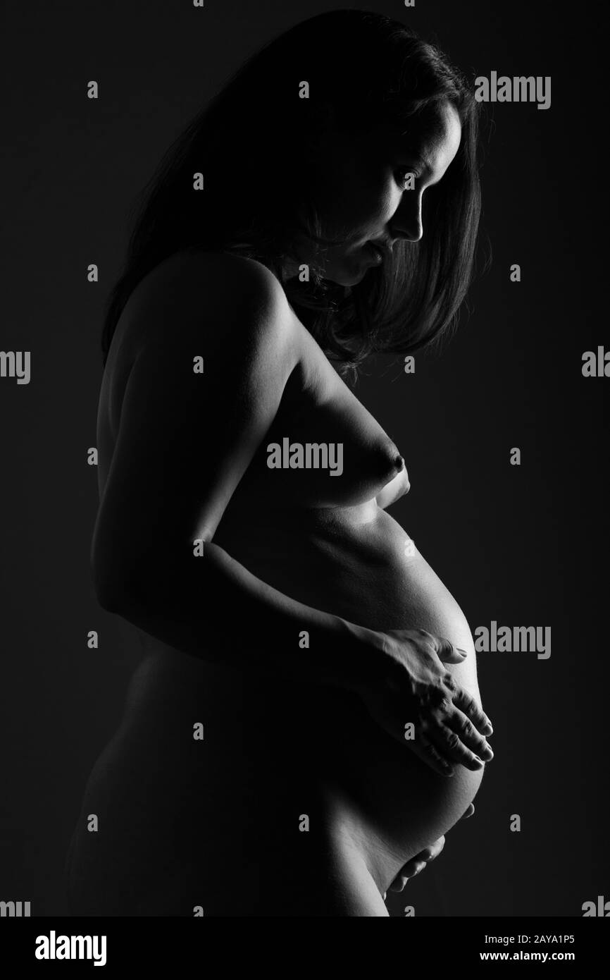 Femme nue enceinte tenant son ventre de bébé. Noir et blanc. Banque D'Images
