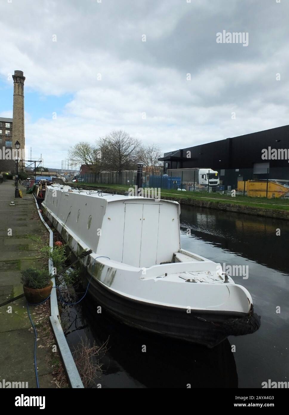 un bateau étroit blanc amarré sur le canal dans une zone industrielle de huddersfield avec pont dans le dis Banque D'Images