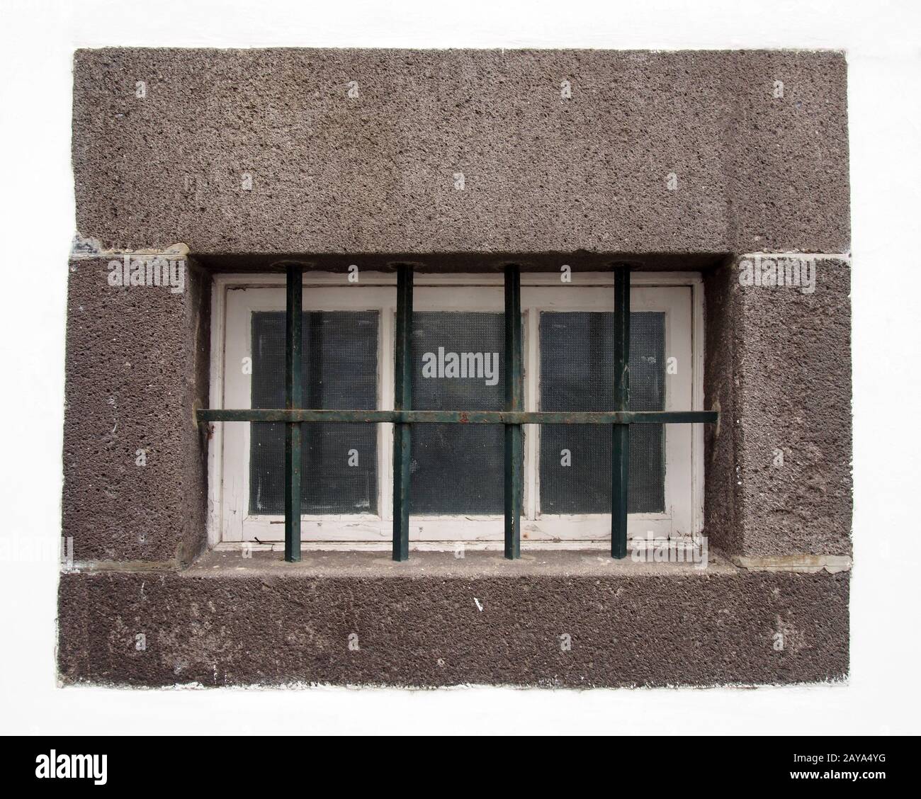 une petite fenêtre en bois blanc avec des panneaux de verre couverts par des barres d'acier dans un grand cadre gris en pierre Banque D'Images