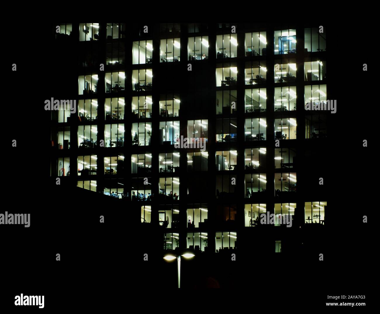 fenêtres lumineuses dans un grand bâtiment moderne de bureau la nuit montrant des espaces de bureau entourés d'obscurité Banque D'Images