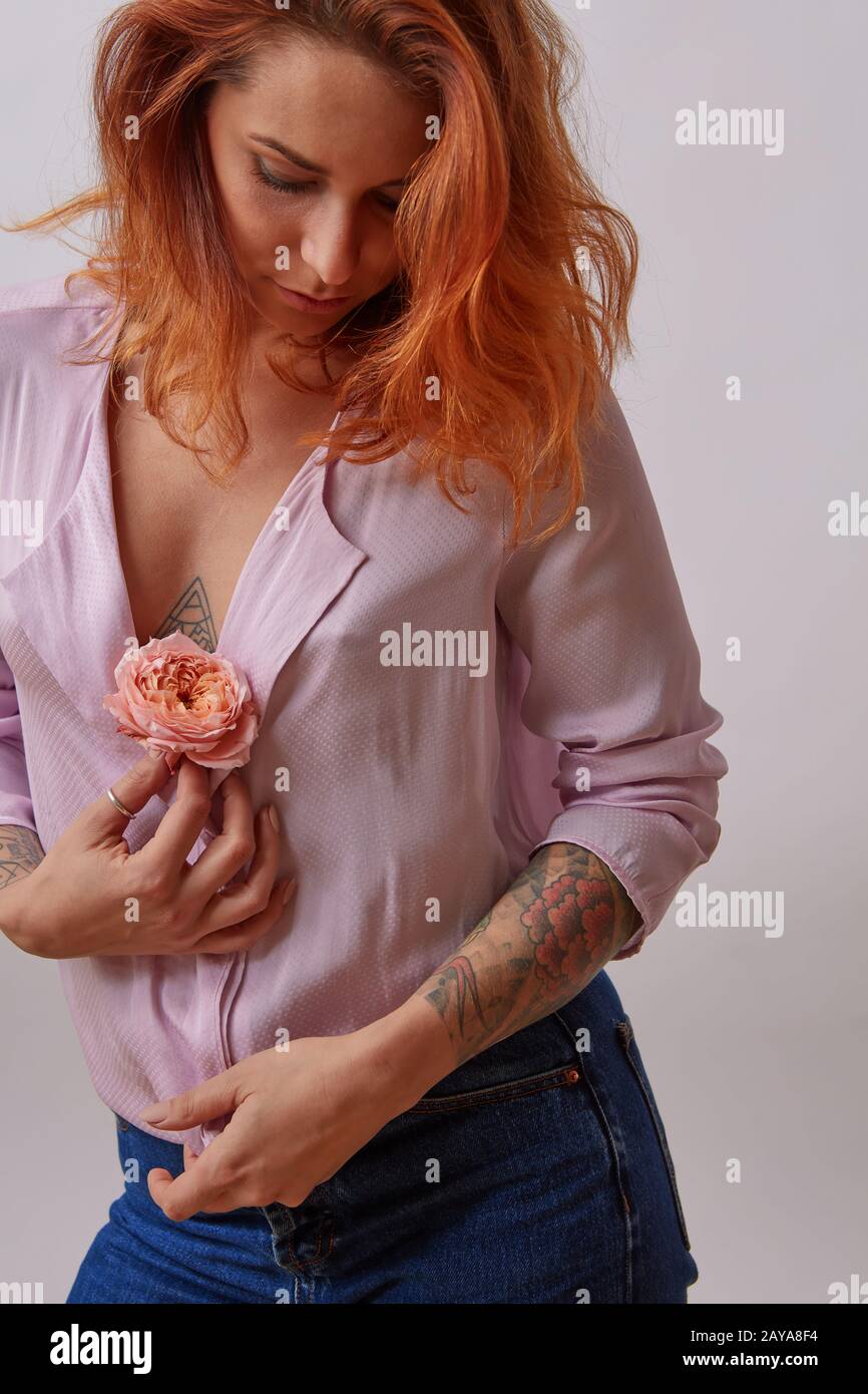 Fille sexuelle à poil rouge avec fleur fraîche vivant couleur corail dans les mains avec tatouage sur un fond gris. Espace de copie. Cadeau sur femme Banque D'Images