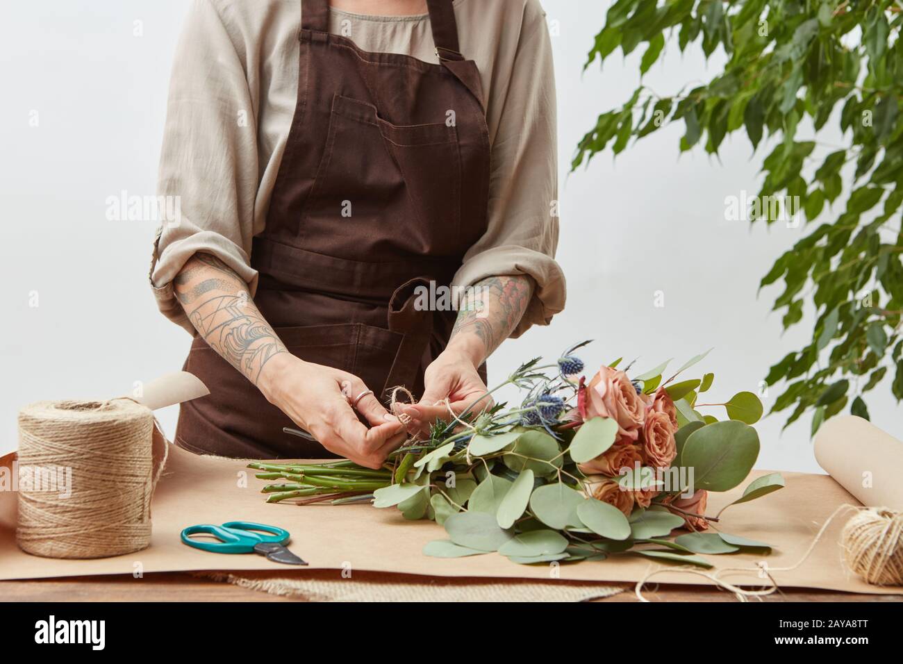La femme fleuriste crée un bouquet de roses fraîches sur un fond gris. Traiter étape par étape. Petite entreprise avec livraison de fleurs. M Banque D'Images