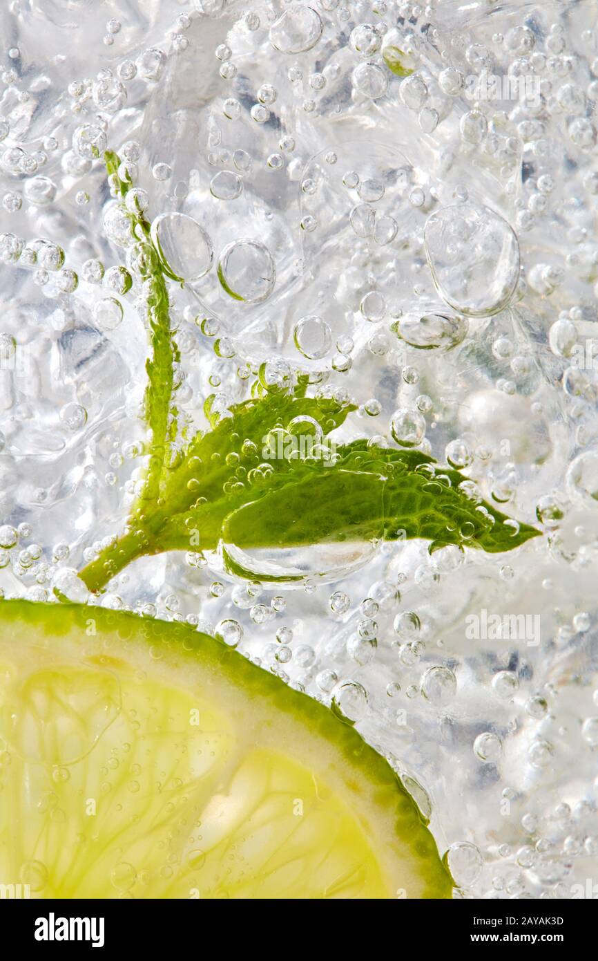 Feuille de menthe fraîche et une tranche de citron vert avec des bulles dans un verre avec de la glace. Macro photo de verre Banque D'Images