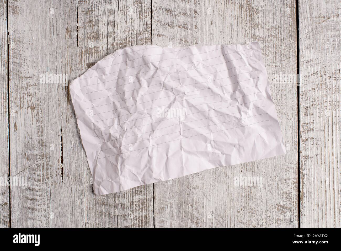 Papier déchiré froissé placé au-dessus d'une table en bois. La feuille demi-cassée s'adhère à l'arrière-plan classique en position inclinée. Façon artistique Banque D'Images