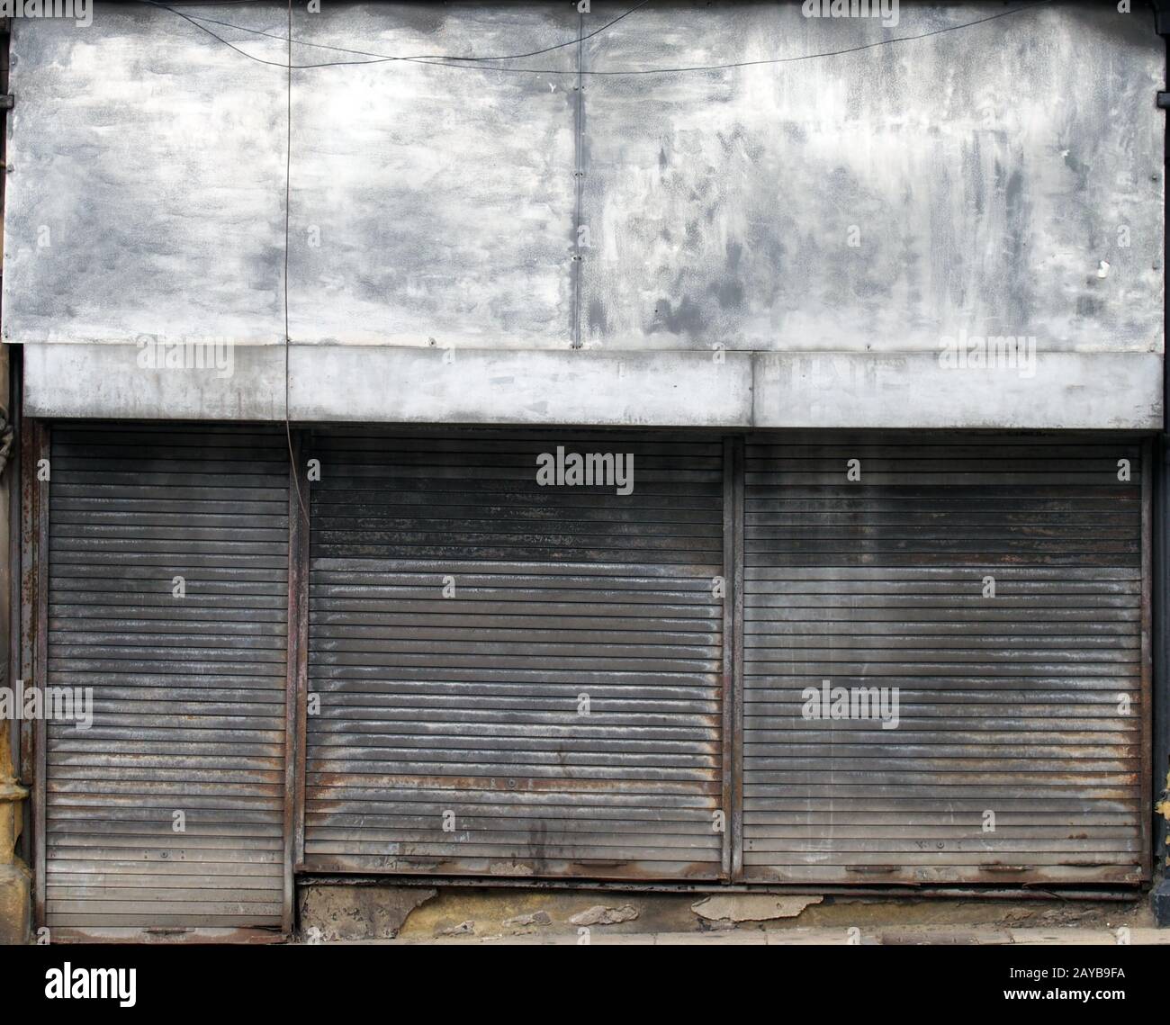 l'avant d'un magasin abandonné dans une rue avec des volets métalliques sales et sales fermés au-dessus de l'avant et de la porte du magasin Banque D'Images
