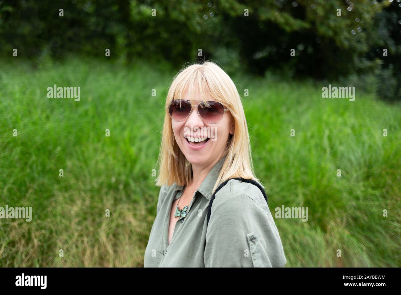 Une femme blonde heureuse souriant devant un fond naturel vert. Été, plein air et style de vie co Banque D'Images