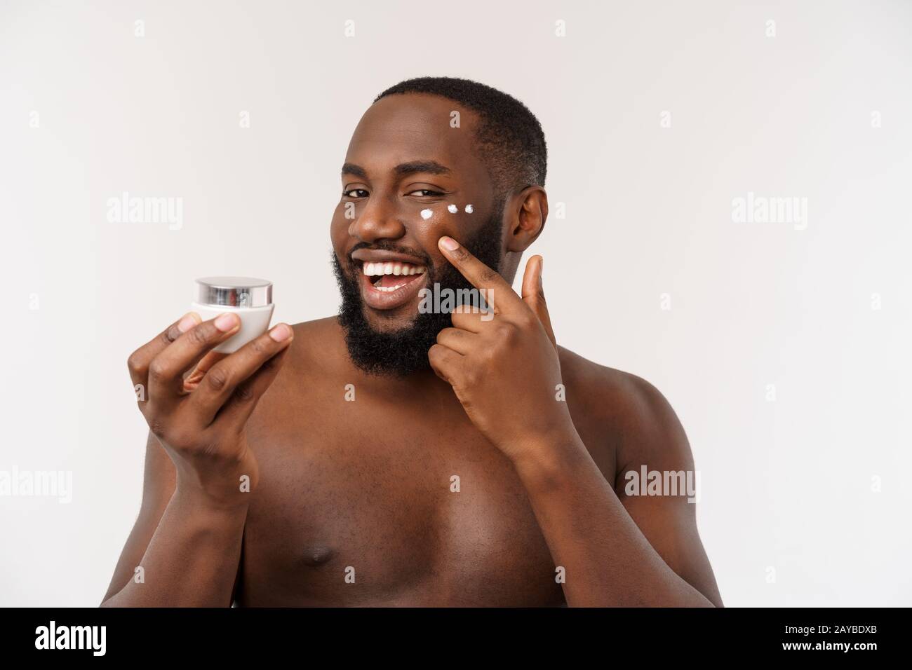 Smiling afro homme l'application de la crème sur son visage. Concept de soins de la peau de l'homme Banque D'Images