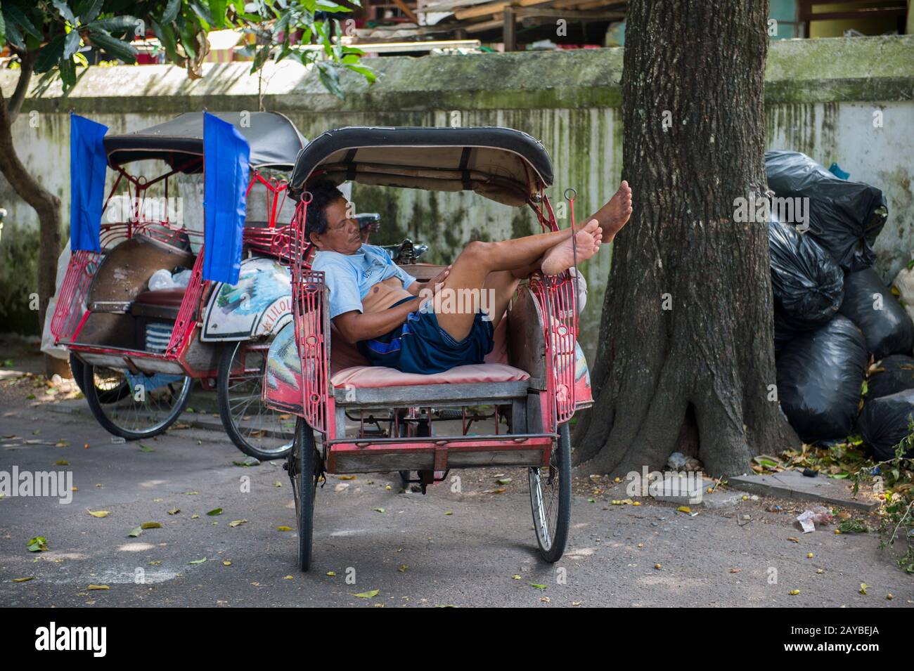 Scène de rue avec un chauffeur de pousse-pousse endormi à Yogyakarta, Java, Indonésie. Banque D'Images