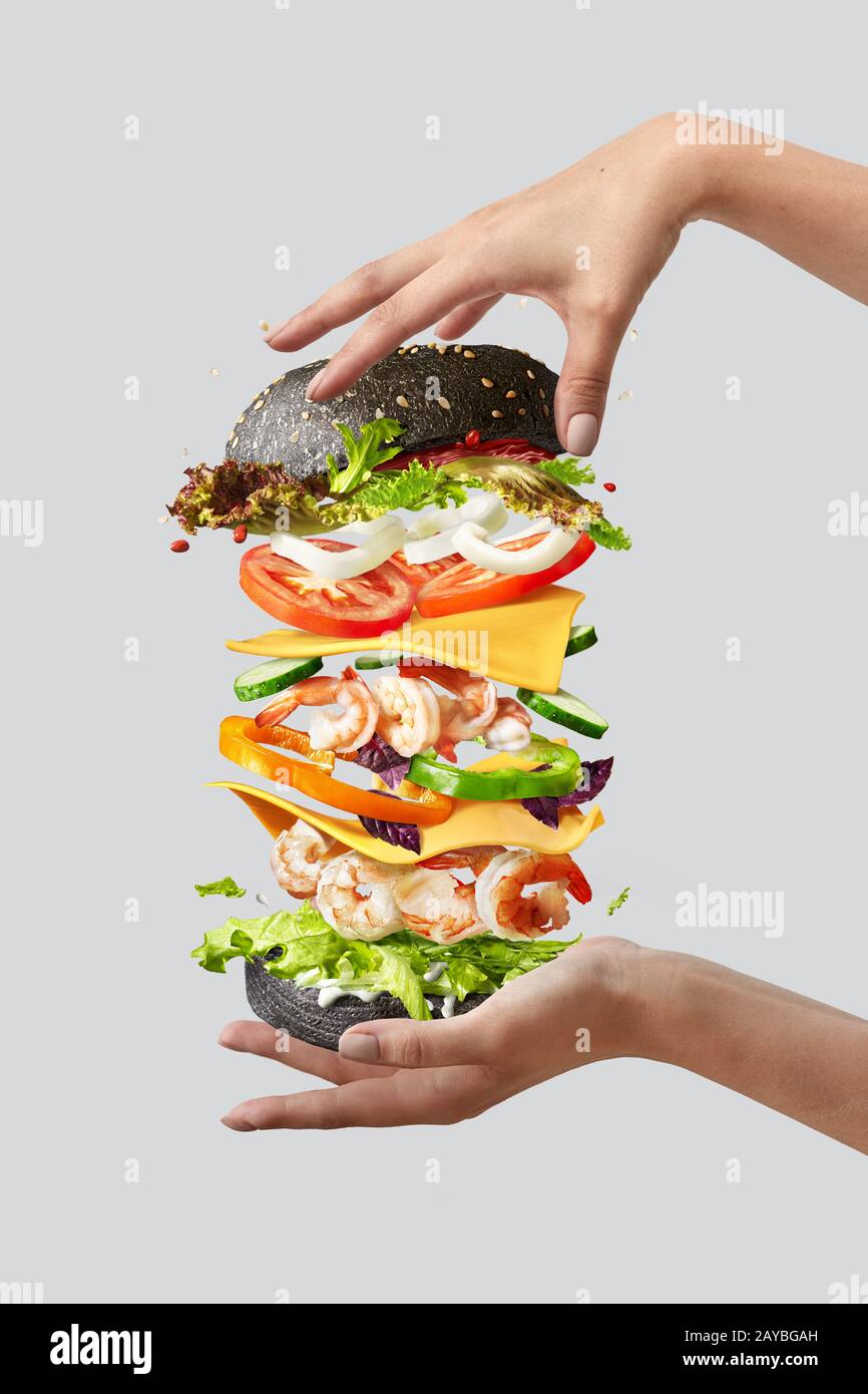 Hamburger volant avec des ingrédients frais entre les mains de la femme sur un fond clair. Banque D'Images