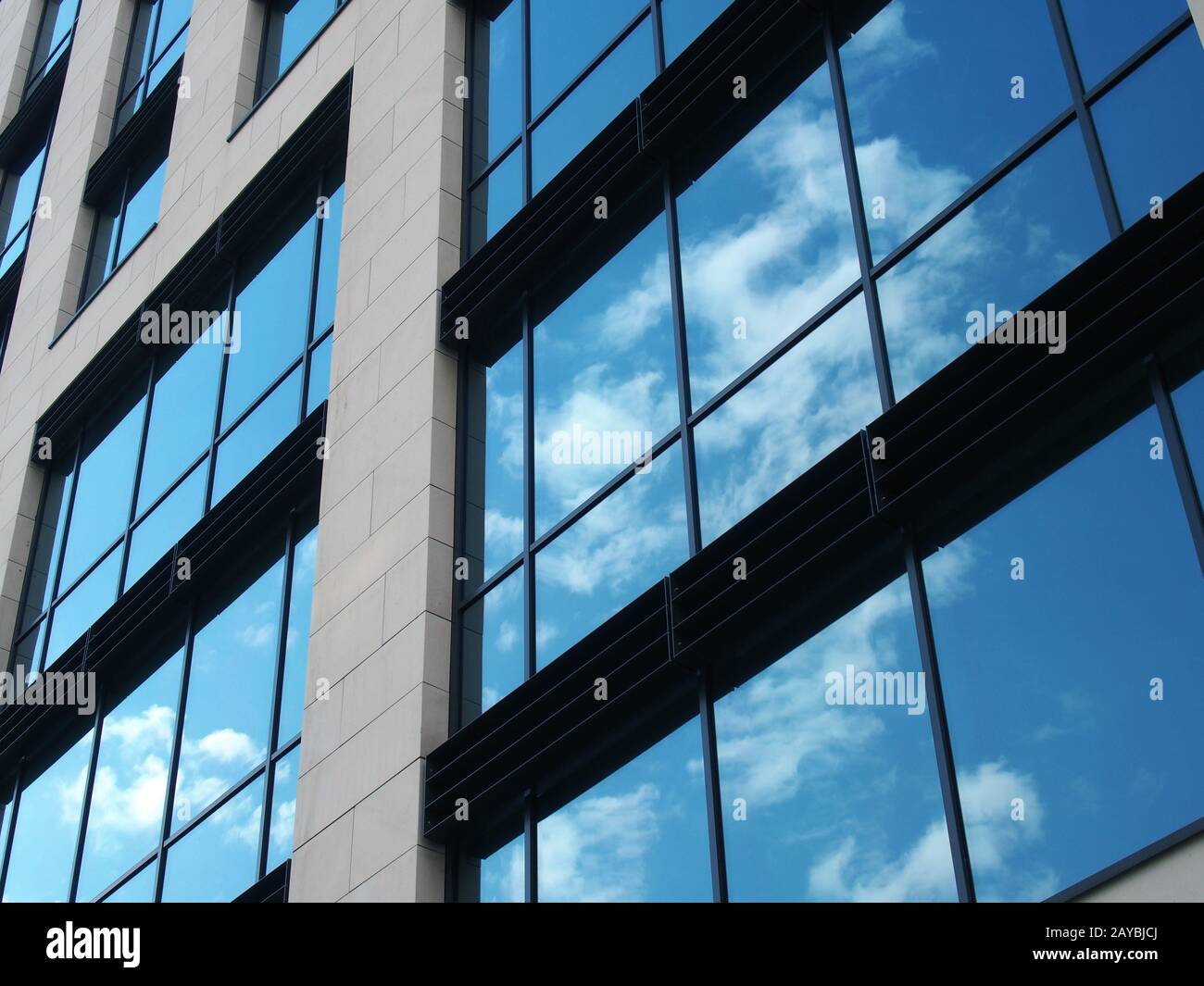vue angulaire d'un bâtiment commercial moderne avec de grandes fenêtres en miroir reflétant le ciel bleu et les nuages blancs Banque D'Images